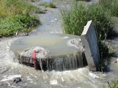 A sewer manhole overflowing, water running over the whole cover and away across the ground